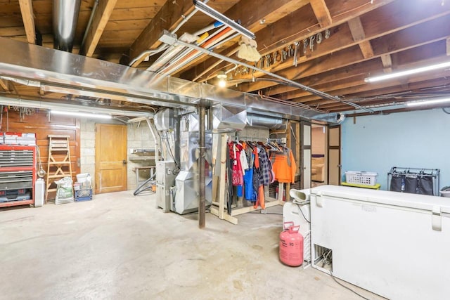 unfinished below grade area featuring heating unit and white fridge