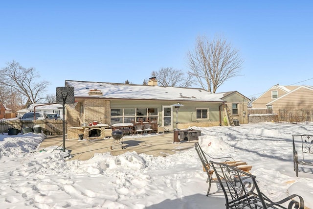 snow covered back of property with brick siding, a chimney, and fence