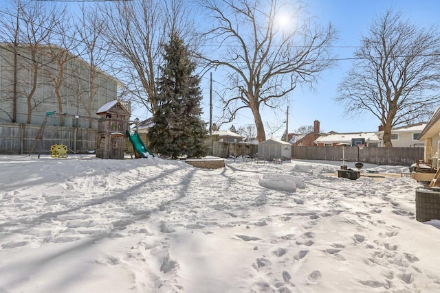 yard layered in snow with an outdoor structure, a playground, a fenced backyard, and a shed