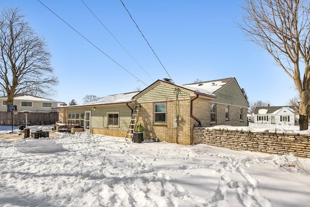 snow covered back of property with fence and brick siding