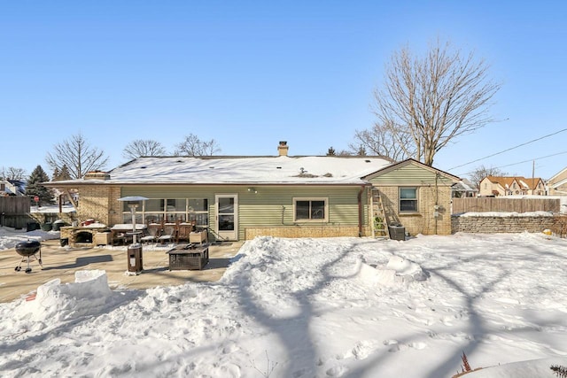 snow covered property with brick siding, a chimney, an outdoor fire pit, and fence