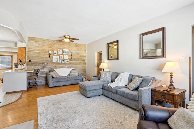 living area with ceiling fan, wooden walls, and wood finished floors