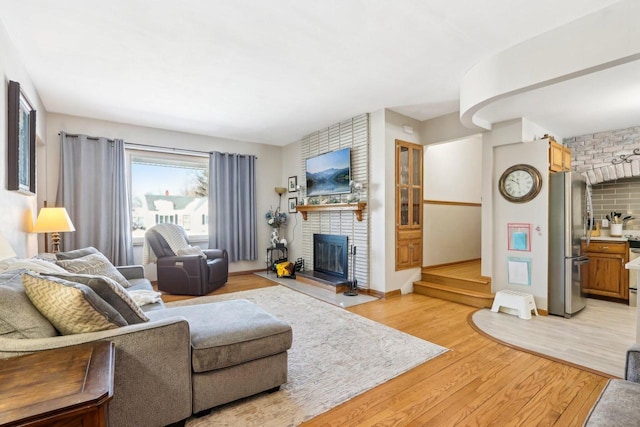 living area with stairs, light wood-style flooring, a fireplace, and baseboards