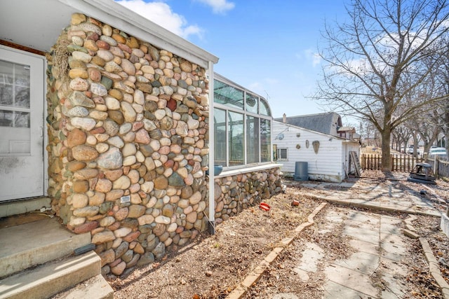 view of home's exterior featuring stone siding, central AC, and fence