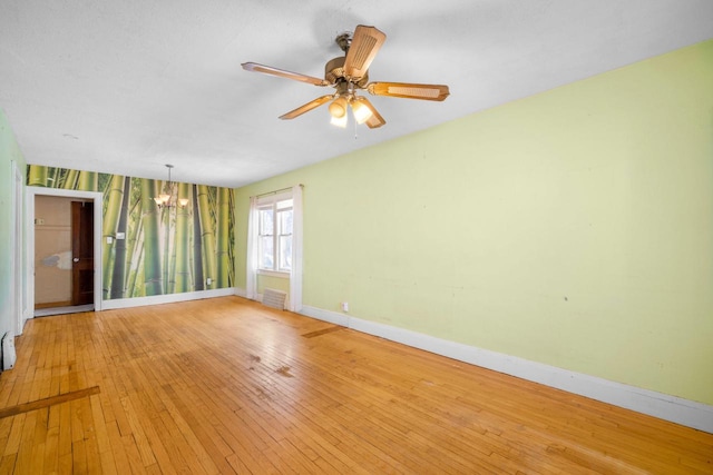 empty room with visible vents, baseboards, ceiling fan with notable chandelier, and light wood finished floors