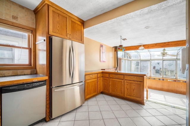 kitchen featuring light tile patterned floors, light countertops, appliances with stainless steel finishes, a textured ceiling, and brown cabinets