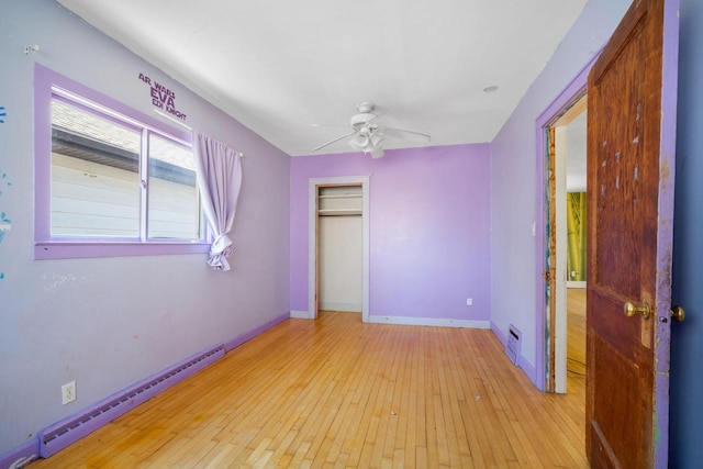 unfurnished bedroom with a baseboard heating unit, ceiling fan, baseboards, hardwood / wood-style flooring, and a closet