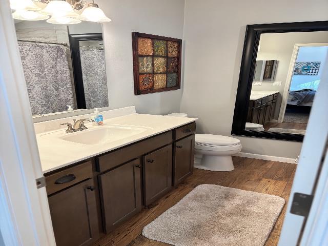 full bath featuring curtained shower, toilet, an inviting chandelier, wood finished floors, and vanity