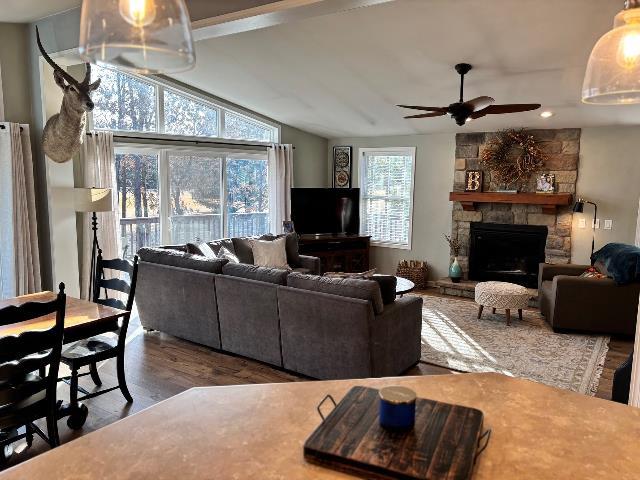 living room with ceiling fan, a stone fireplace, wood finished floors, and vaulted ceiling