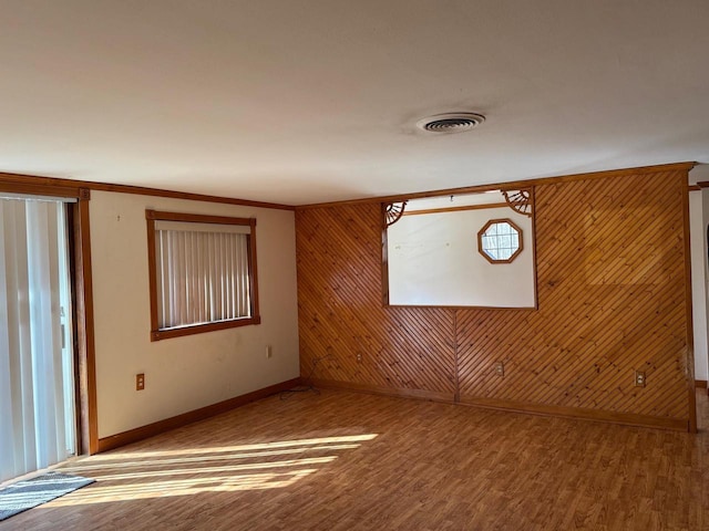 spare room featuring visible vents, wood walls, baseboards, and wood finished floors