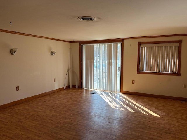 spare room featuring baseboards, wood finished floors, visible vents, and ornamental molding