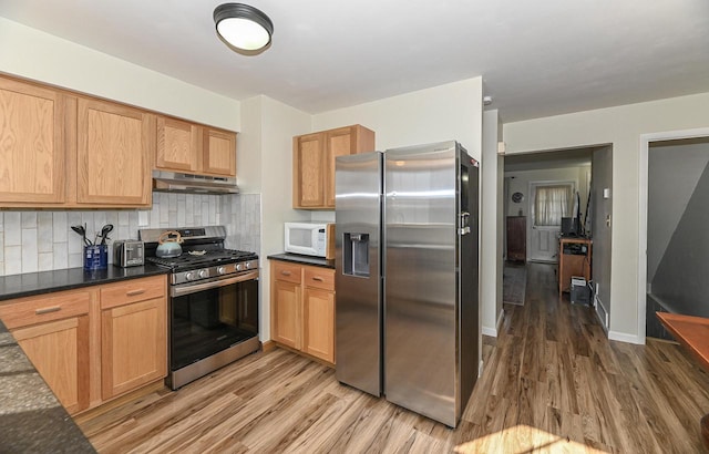 kitchen with under cabinet range hood, tasteful backsplash, appliances with stainless steel finishes, and light wood finished floors