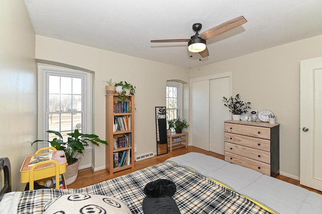 bedroom with wood finished floors, visible vents, baseboards, arched walkways, and a closet