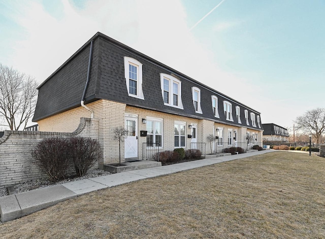 townhome / multi-family property featuring a front yard, mansard roof, brick siding, and a shingled roof