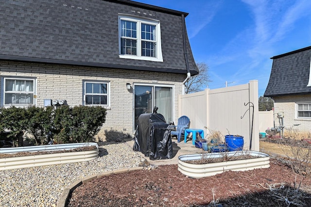 back of property with mansard roof, brick siding, roof with shingles, and fence