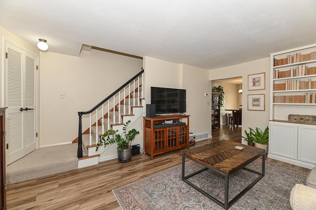 living room featuring stairway, visible vents, baseboards, and wood finished floors