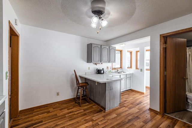 kitchen with a breakfast bar, light countertops, gray cabinets, a peninsula, and wood finished floors