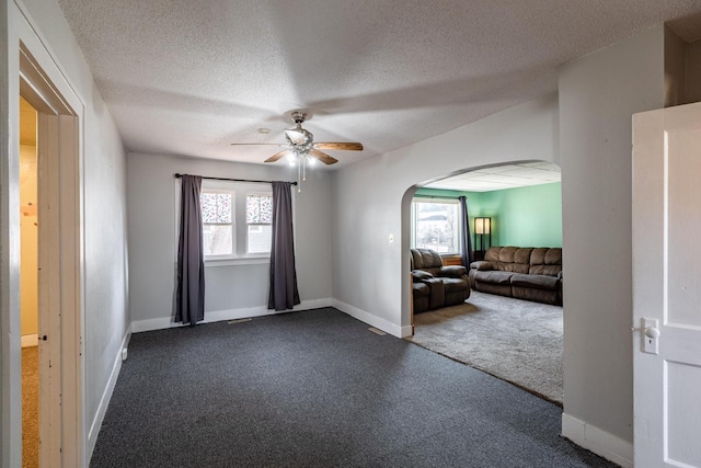 empty room with arched walkways, dark carpet, baseboards, and a ceiling fan