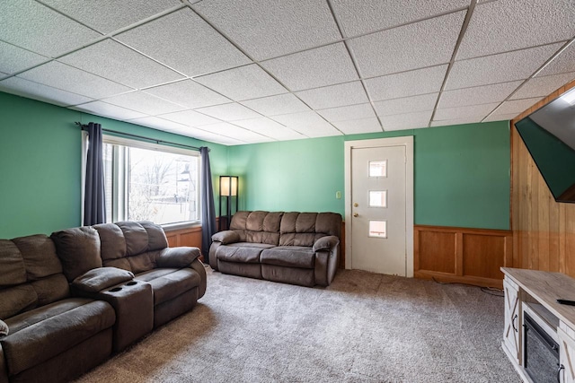 carpeted living area with a paneled ceiling and a wainscoted wall