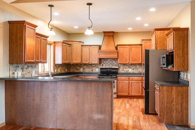 kitchen with premium range hood, dark countertops, stainless steel appliances, light wood-style floors, and a peninsula