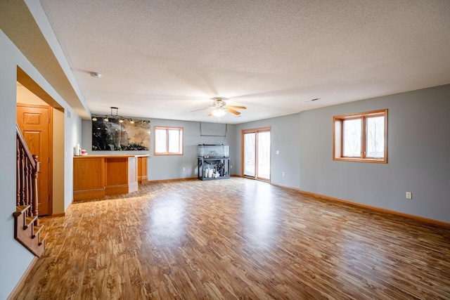 unfurnished living room with a textured ceiling, stairway, light wood finished floors, baseboards, and ceiling fan