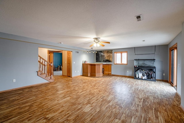 unfurnished living room featuring visible vents, a textured ceiling, stairway, light wood-style floors, and baseboards