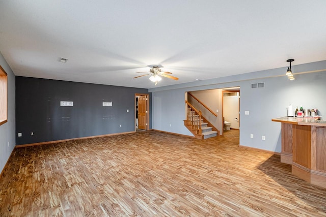 unfurnished living room featuring stairway, wood finished floors, visible vents, and baseboards