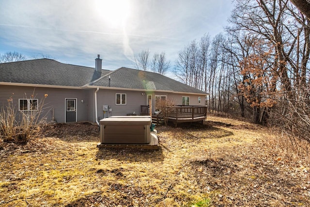 rear view of house with a shingled roof, a wooden deck, a chimney, and a hot tub