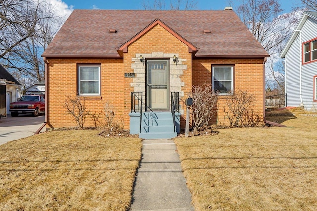 bungalow featuring brick siding, a shingled roof, and a front yard