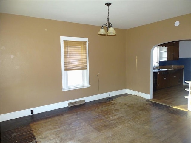 unfurnished dining area with arched walkways, dark wood-style floors, and baseboards