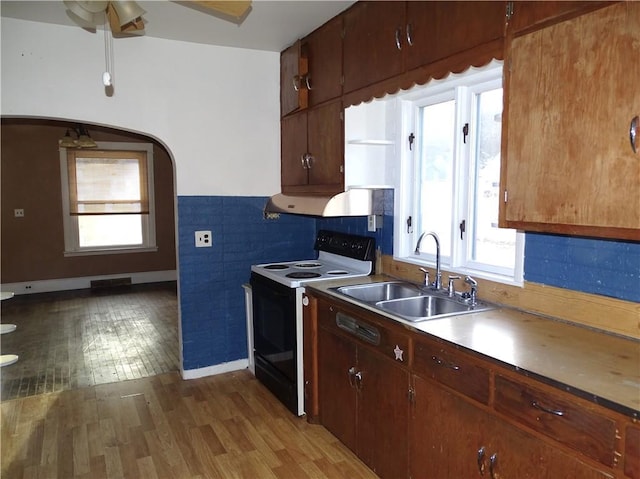 kitchen featuring wood finished floors, electric range, arched walkways, a sink, and under cabinet range hood