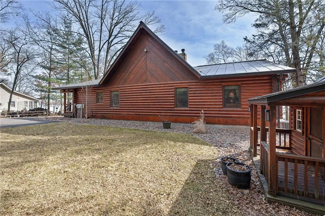 view of side of property featuring a standing seam roof, a yard, metal roof, log siding, and a chimney