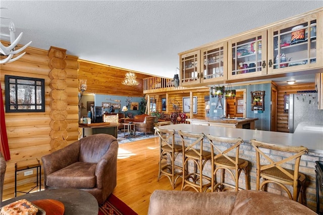 bar featuring a chandelier, log walls, freestanding refrigerator, wood finished floors, and a textured ceiling