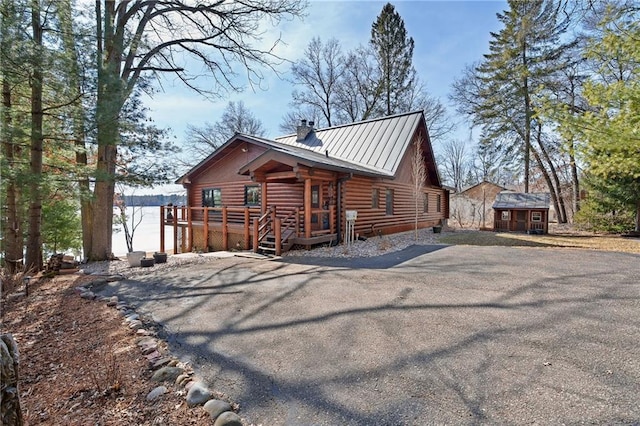 view of front of property with a standing seam roof, metal roof, an outdoor structure, log siding, and a chimney