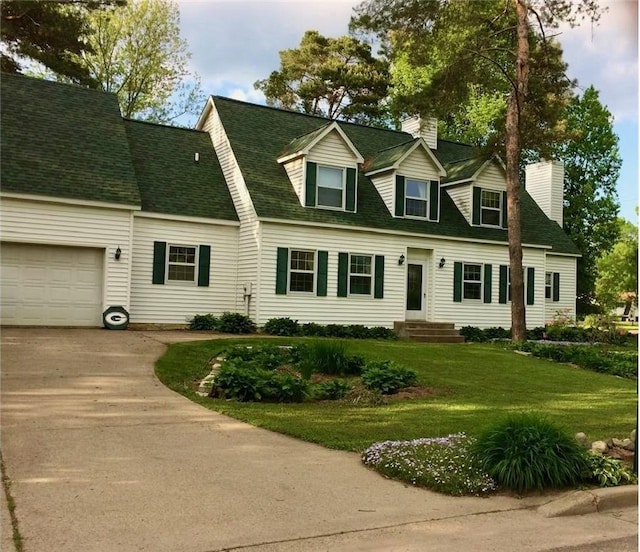 cape cod home featuring driveway, roof with shingles, a front yard, a garage, and a chimney