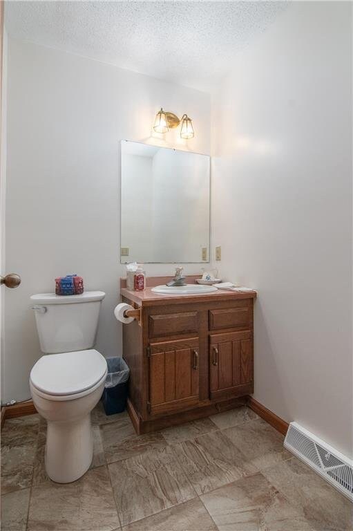 227 Donatelle St, Amery, WI 54001 - bathroom featuring visible vents, toilet, a textured ceiling, baseboards, and vanity