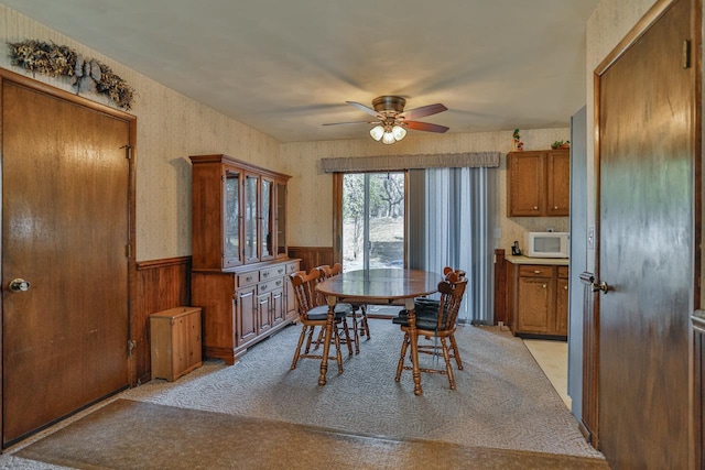 dining room with light carpet, a wainscoted wall, wallpapered walls, and ceiling fan