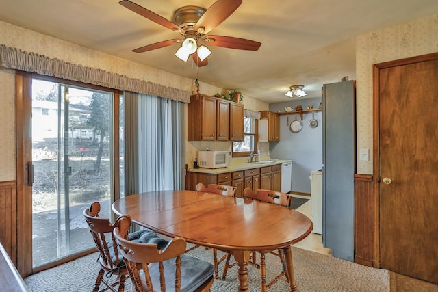 dining space featuring wallpapered walls, a ceiling fan, and a wainscoted wall