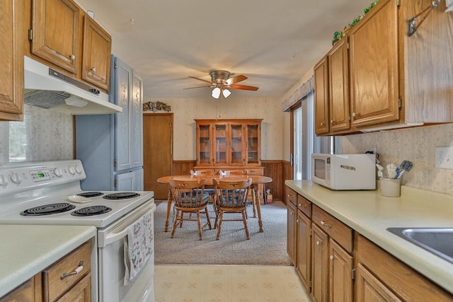 kitchen featuring under cabinet range hood, wallpapered walls, white appliances, wainscoting, and light countertops