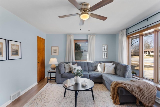 living room featuring visible vents, baseboards, light wood-style flooring, and a ceiling fan