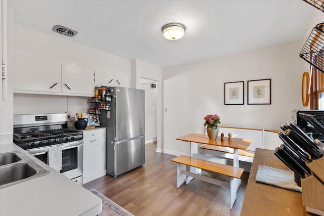 kitchen with visible vents, a sink, wood finished floors, appliances with stainless steel finishes, and white cabinets