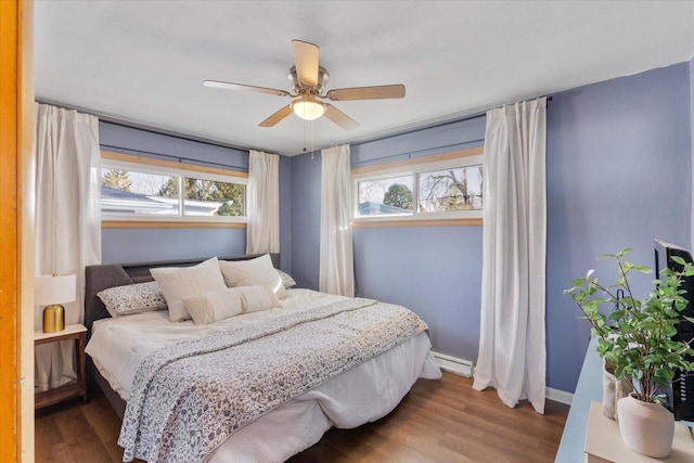 bedroom featuring a baseboard heating unit, multiple windows, baseboards, and wood finished floors