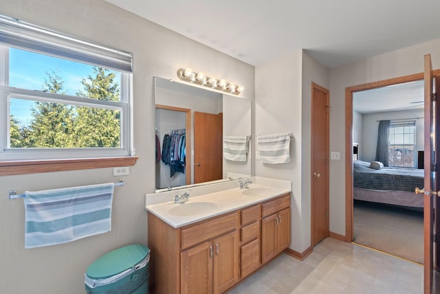 ensuite bathroom with double vanity, connected bathroom, baseboards, and a sink