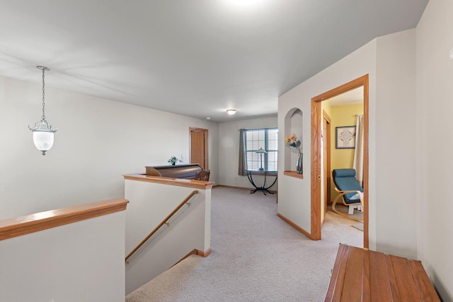 hallway with an upstairs landing, light colored carpet, and baseboards