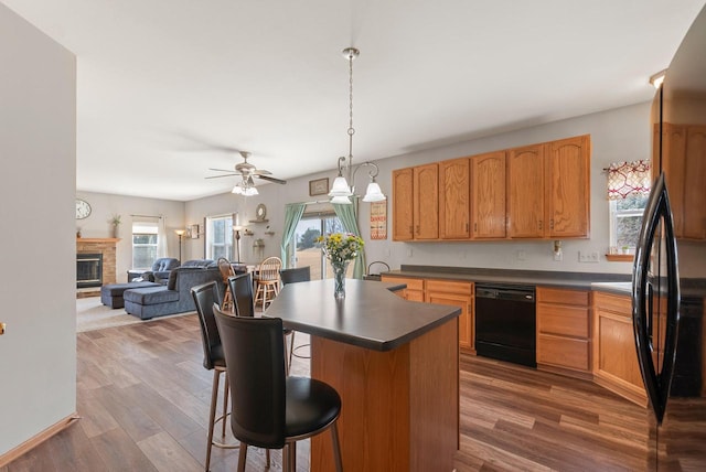 kitchen with a stone fireplace, dark countertops, black appliances, and wood finished floors