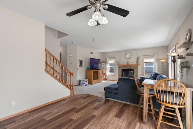 living room with a ceiling fan, a glass covered fireplace, wood finished floors, baseboards, and stairs