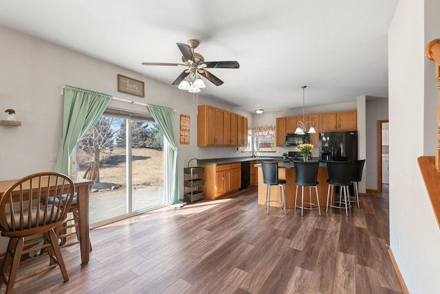 kitchen with dark wood finished floors, black appliances, a kitchen breakfast bar, and dark countertops