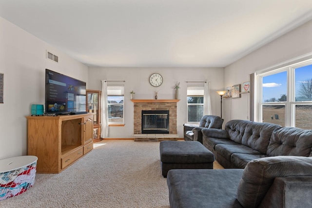 living area featuring a wealth of natural light, visible vents, a glass covered fireplace, and carpet flooring