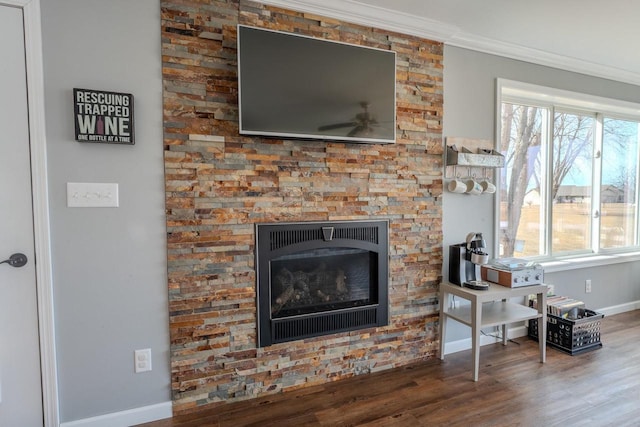 living room featuring a glass covered fireplace, wood finished floors, baseboards, and ornamental molding