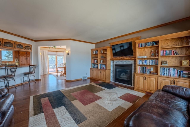 living room featuring visible vents, a glass covered fireplace, wood finished floors, crown molding, and baseboards